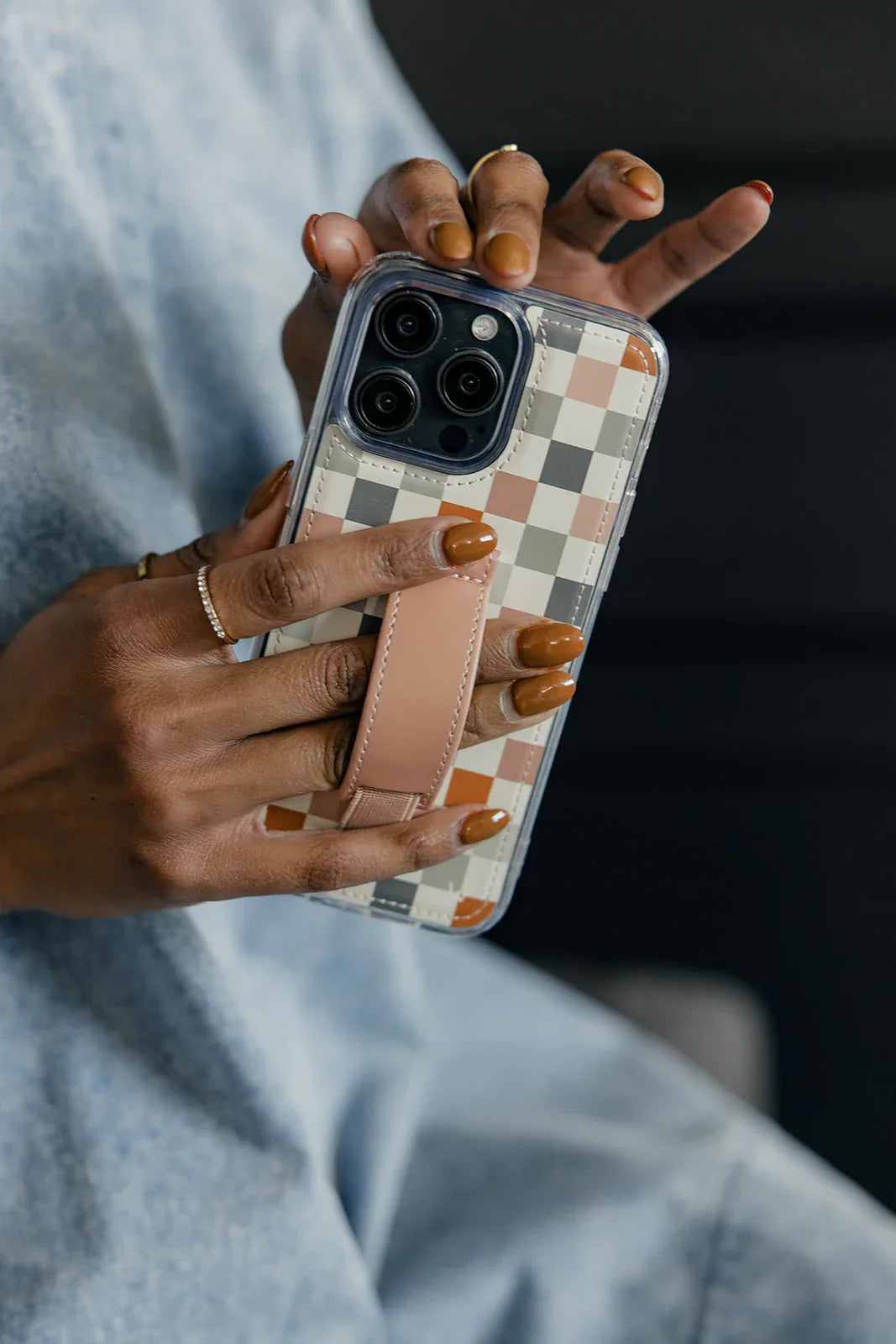 Check pattern phone case with tan strap, held up by hand