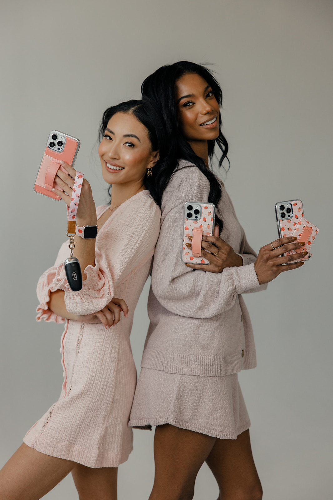 Two strawberry-pattern wrist lanyards holding phones with gold clips