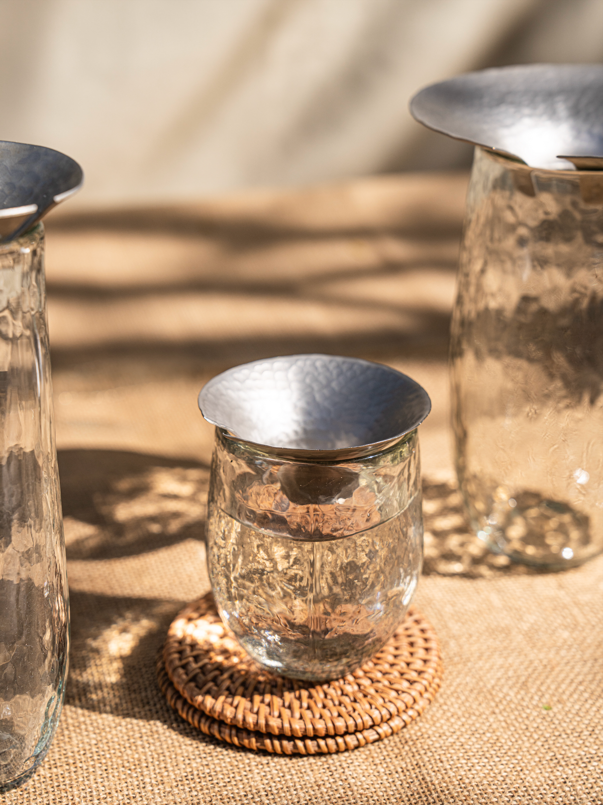 Set of 3 hammered glass propagation vases with silver lids on a woven mat