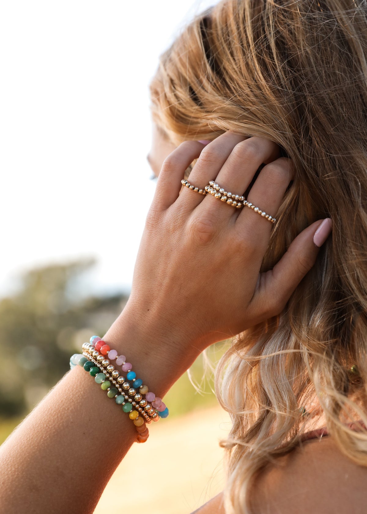 Woman wearing rainbow gemstone beaded bracelet on wrist with gold-tone toggle clasp
