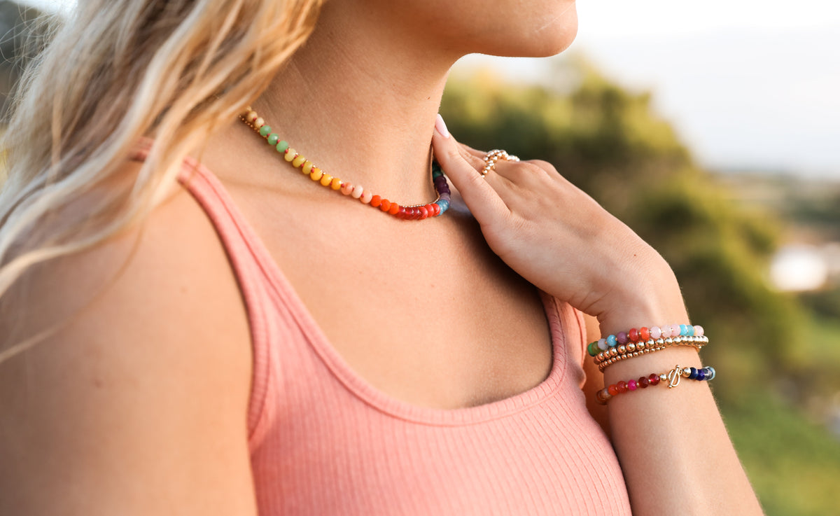 Woman wearing rainbow gemstone beaded bracelets stacked on wrist with gold-tone clasps