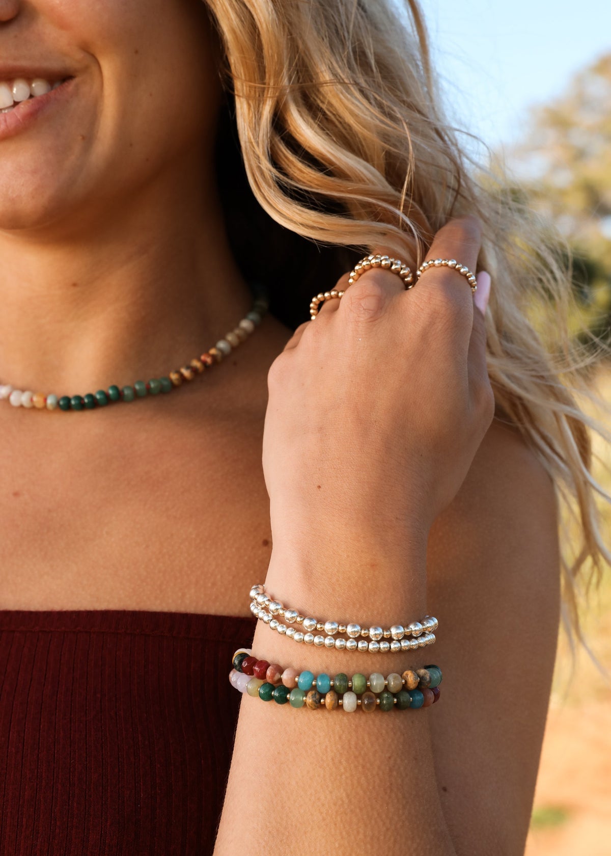 Multi-color gemstone beaded necklace with gold accents and stacked bracelets, worn.