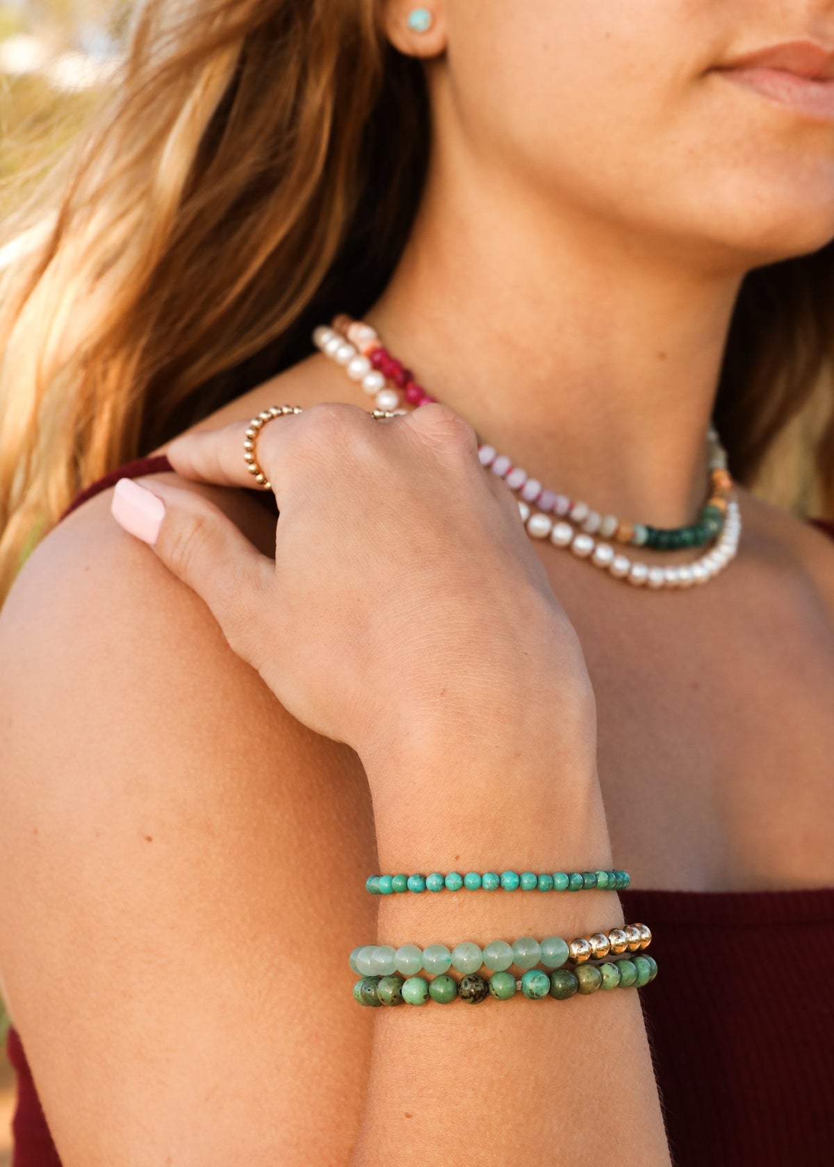 Gemstone beaded necklace with gold accents and stacked multicolor bracelets, close-up.