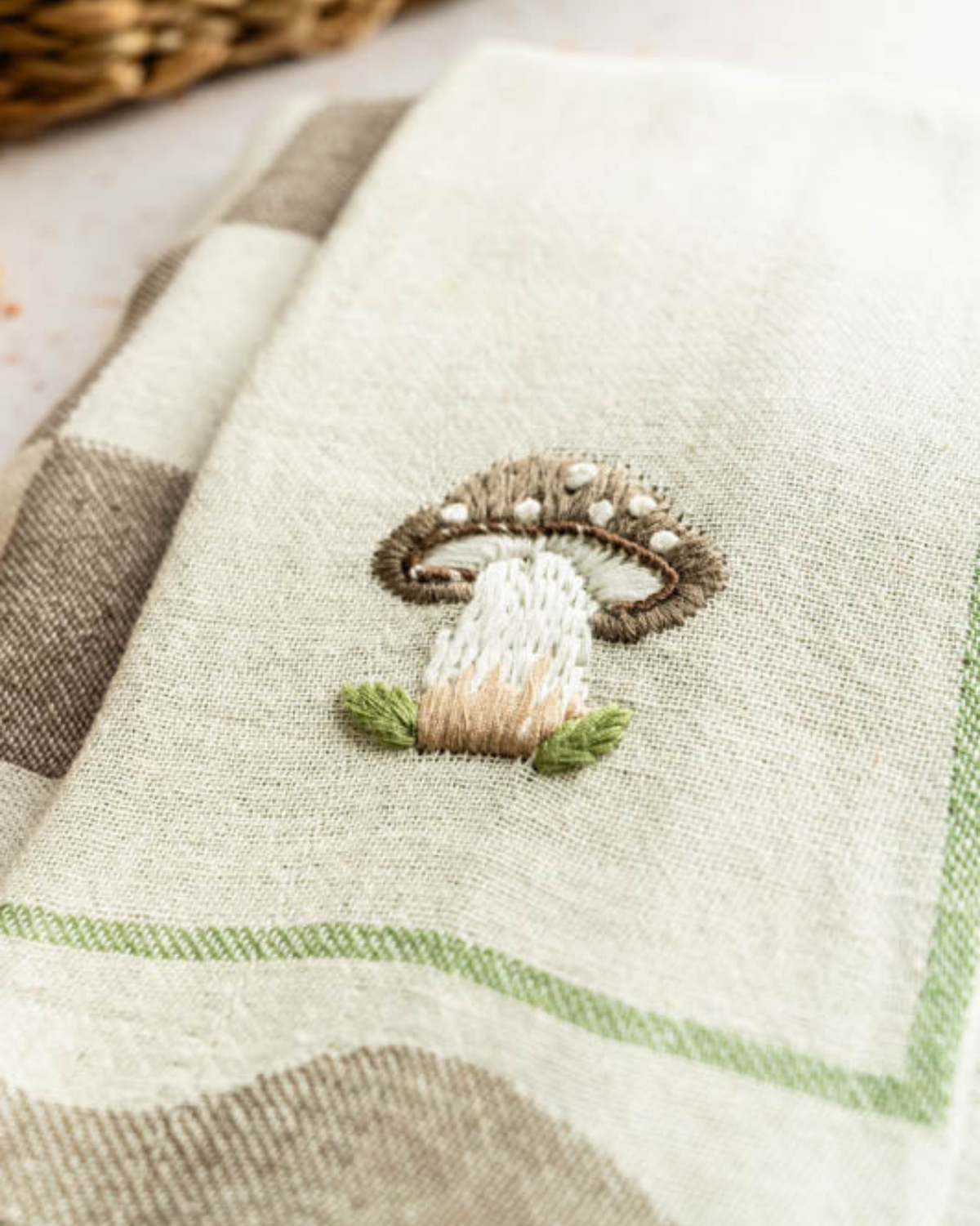 Beige tea towel with centered embroidered mushroom and green striped border, fringed