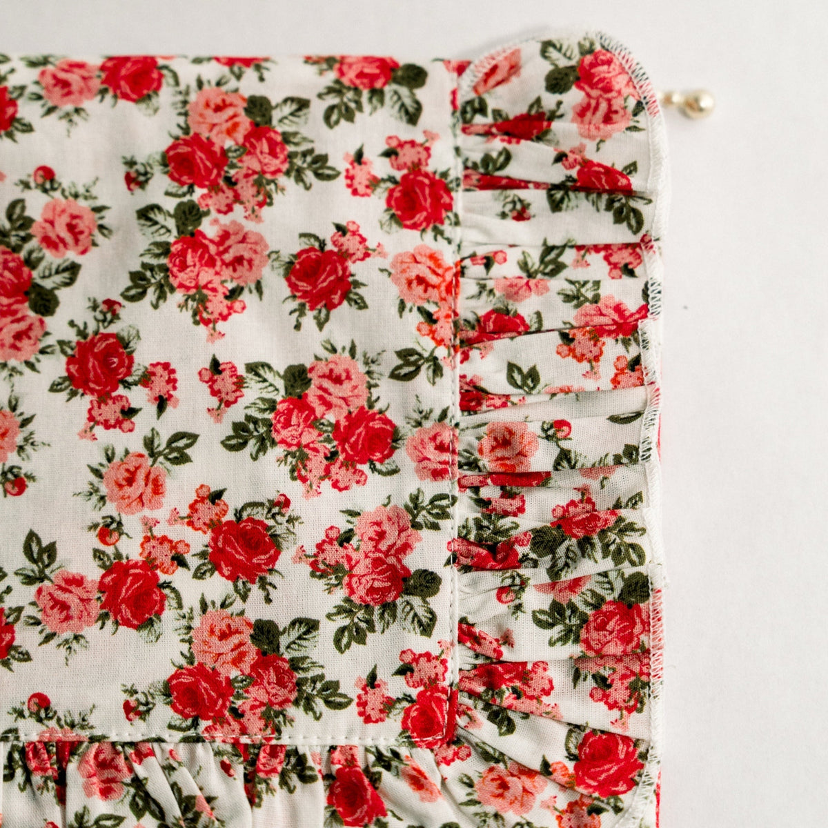 Detail view of floral ruffle pouch showing zipper edge, gathered trim, and gold pull