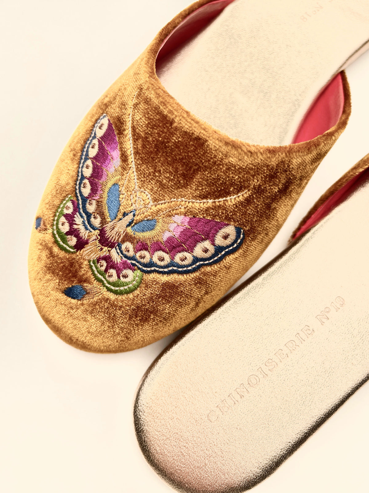Close-up of antique gold velvet mules with colorful butterfly embroidery