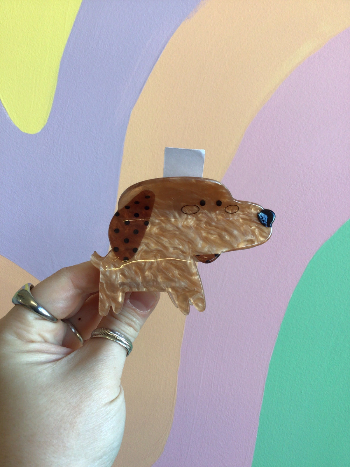 Dog-shaped hair claw in tan with black spots, translucent tail, held in hand