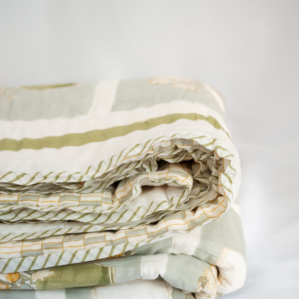 Close-up of folded quilt layers with green-and-white stripes and yellow grid stitching