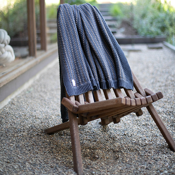 Blue striped knit throw blanket folded and placed on a wooden bench