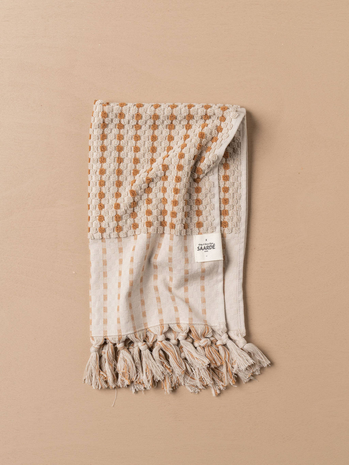 Turkish hand towel folded with terracotta dotted grid, stone stripes, and tassel ends