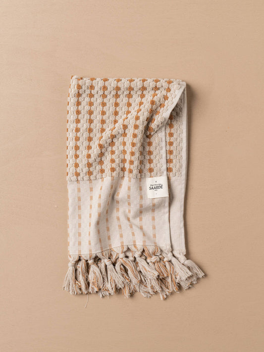 Turkish hand towel folded with terracotta dotted grid, stone stripes, and tassel ends
