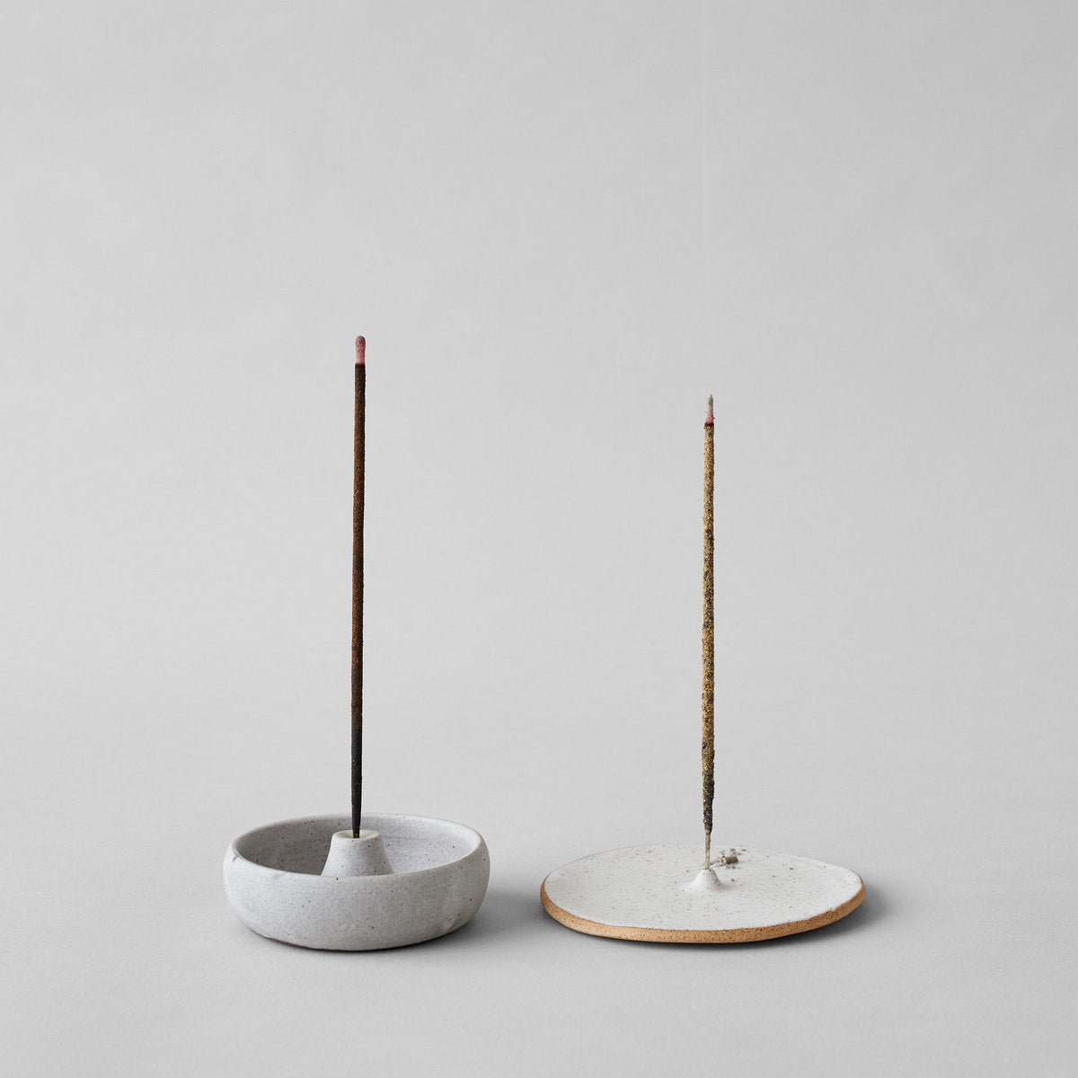 Two incense holders: speckled round base and dark stone base with sticks