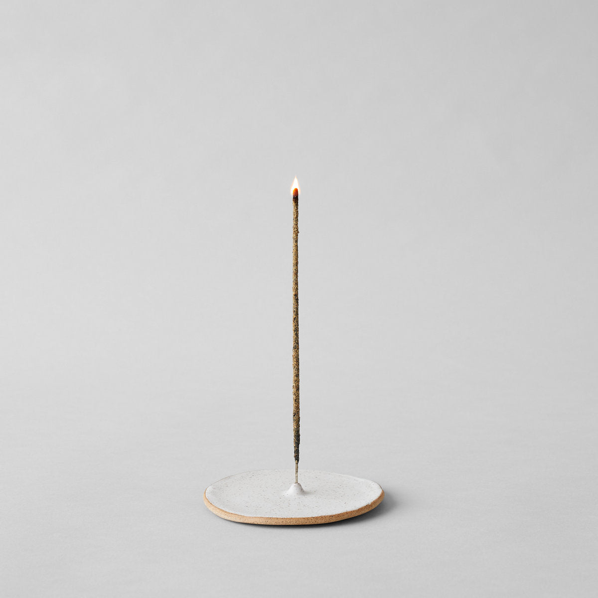 Speckled incense holder with upright incense stick burning flame