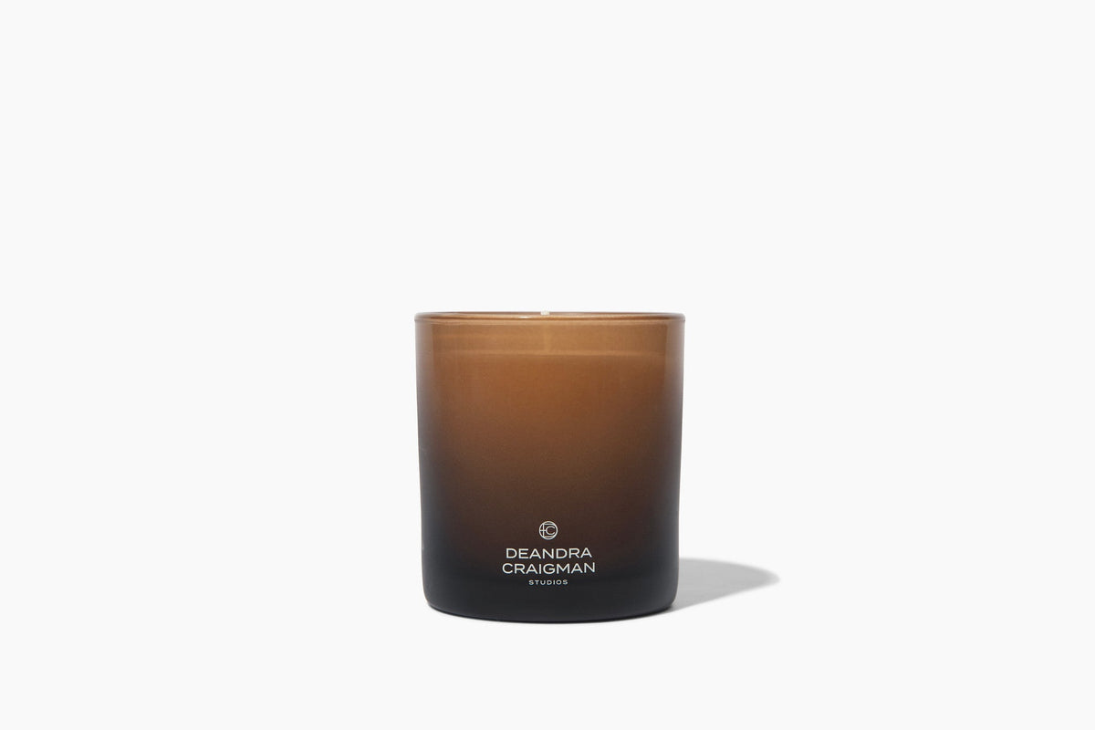 Amber glass jar candle with black base and Deandra Craigman logo on front