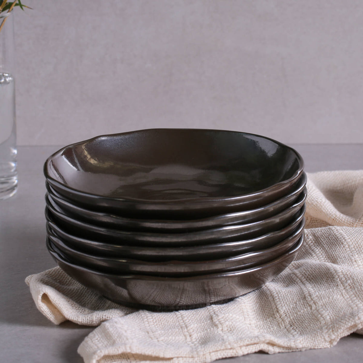 Stack of dark ceramic pasta plates with glossy reactive glaze and curved flared rims.