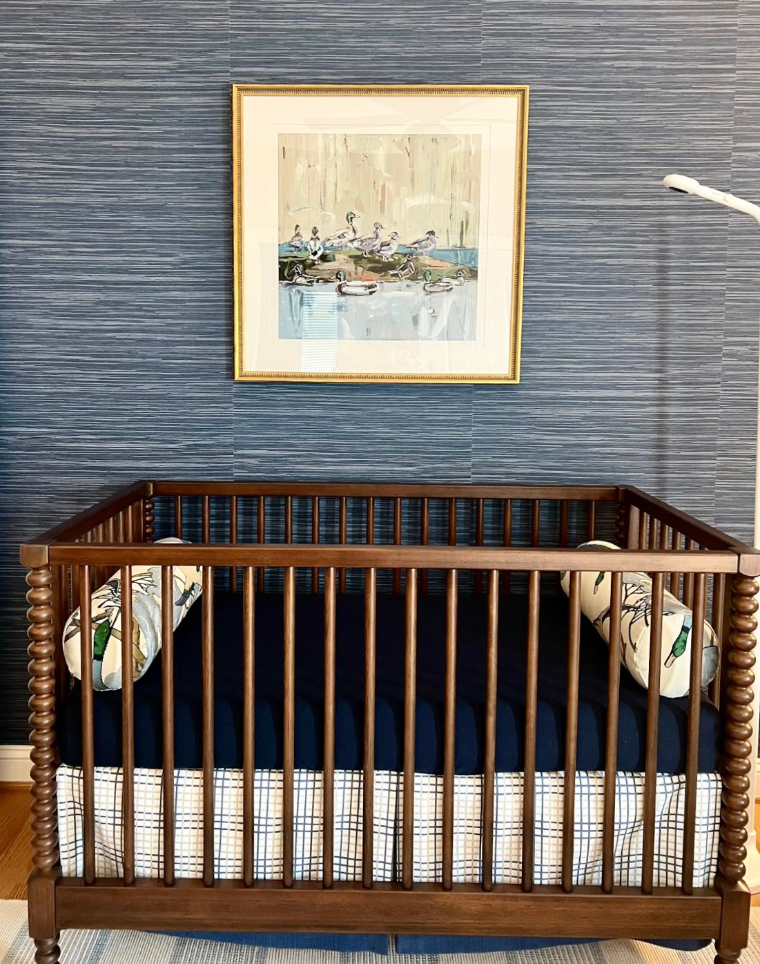 Duck-themed fine art print in gold frame, small white mat, wall and crib in view.