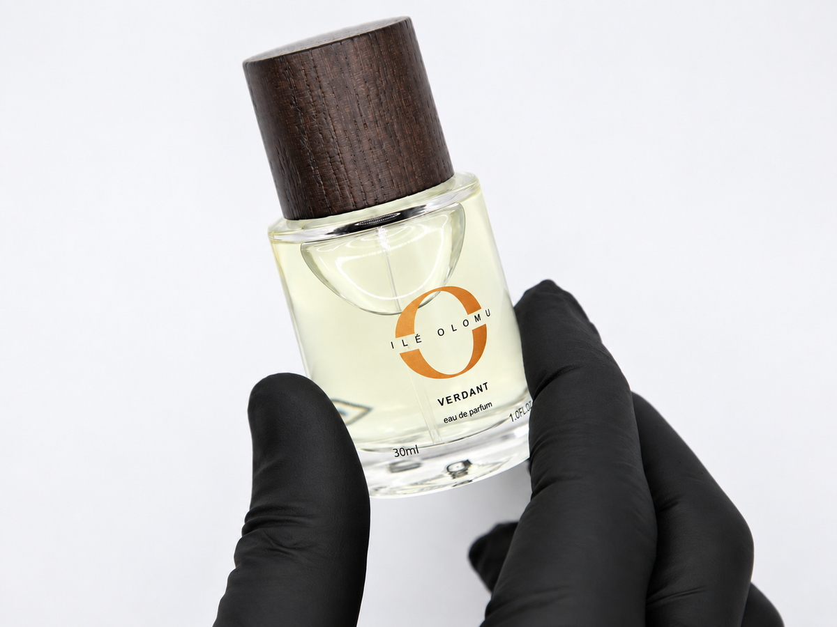 Eau de parfum bottle held by black-gloved hands, dark wood cap