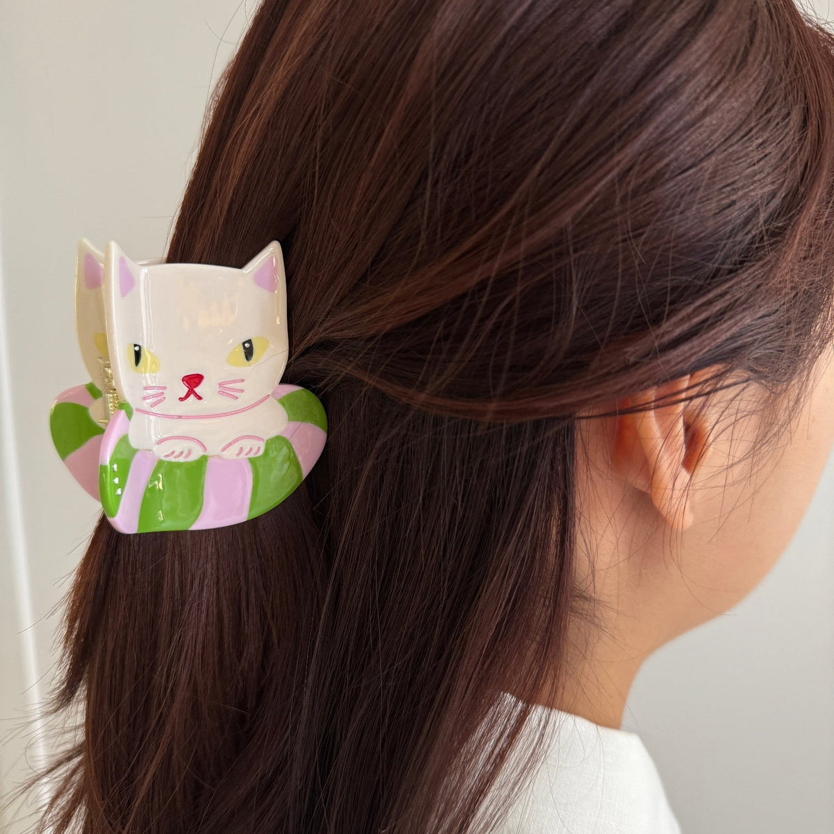 Cat hair claw clip clipped in brown hair, showing white face and green body