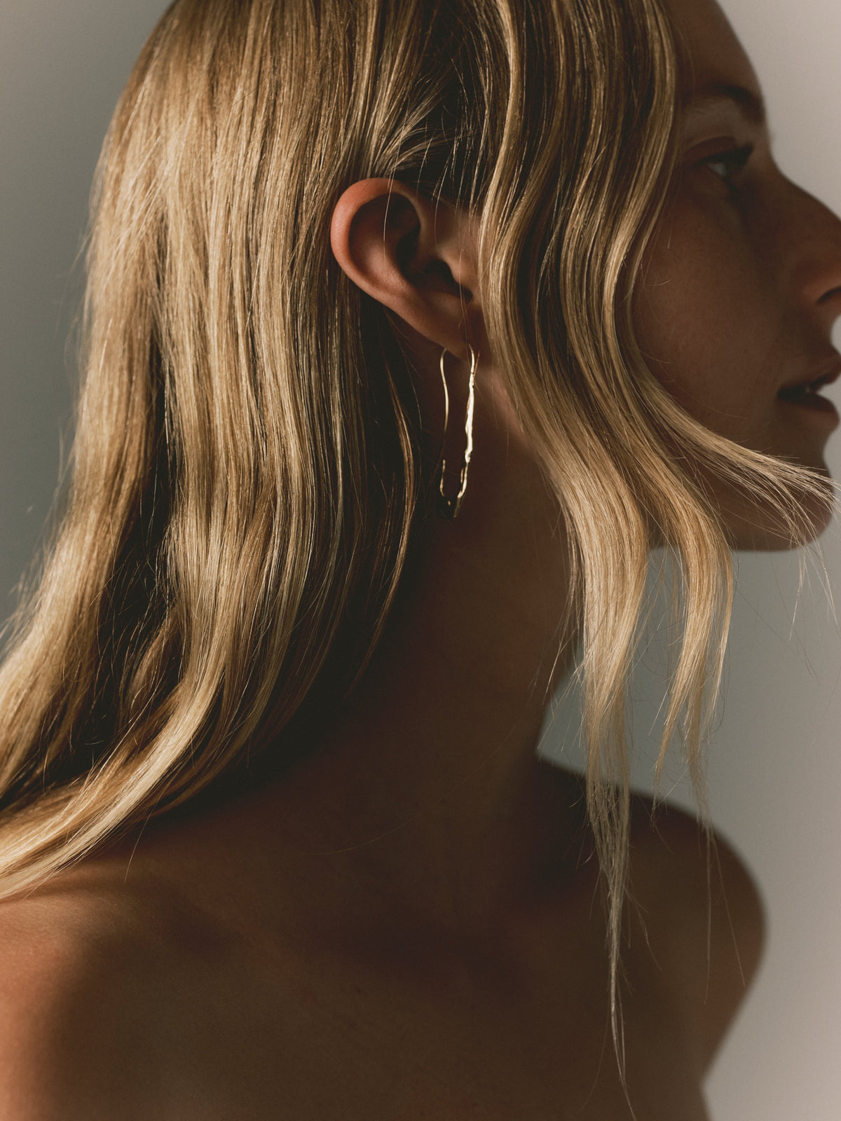 Gold paperclip earrings with hook back, elongated wavy drop seen from side
