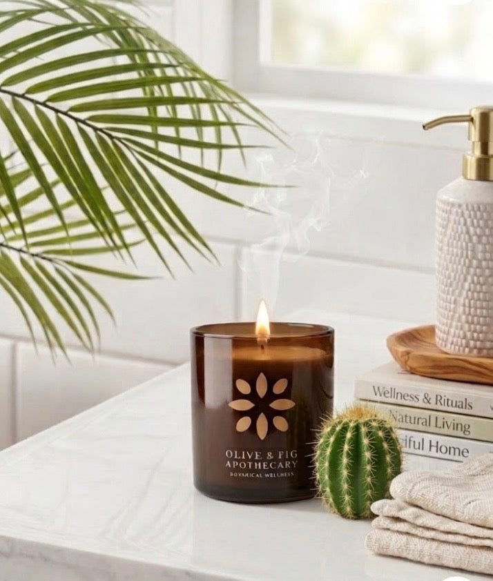 Burning amber glass candle with botanical flower emblem on a light countertop