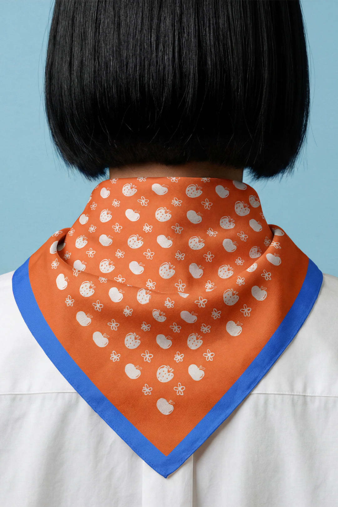 Orange cotton bandana worn at back of neck, blue border with white tiny fruit design.