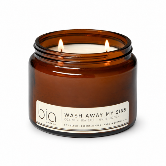 Amber candle jar with lid, lit flame, "Wash Away My Sins" label and bia logo