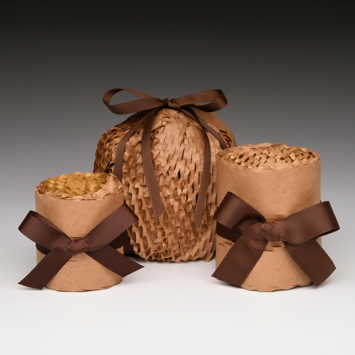 Three kraft paper wrapped candles with brown ribbon bows and woven basket wrap