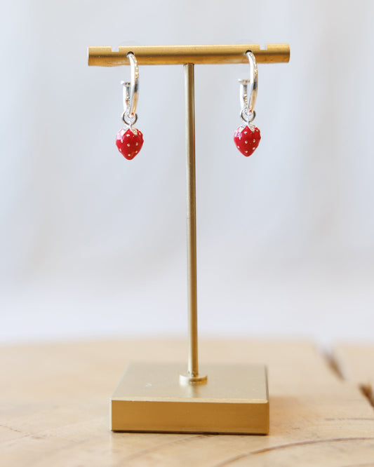 Silver hoop earrings with red strawberry charm dangles on display stand