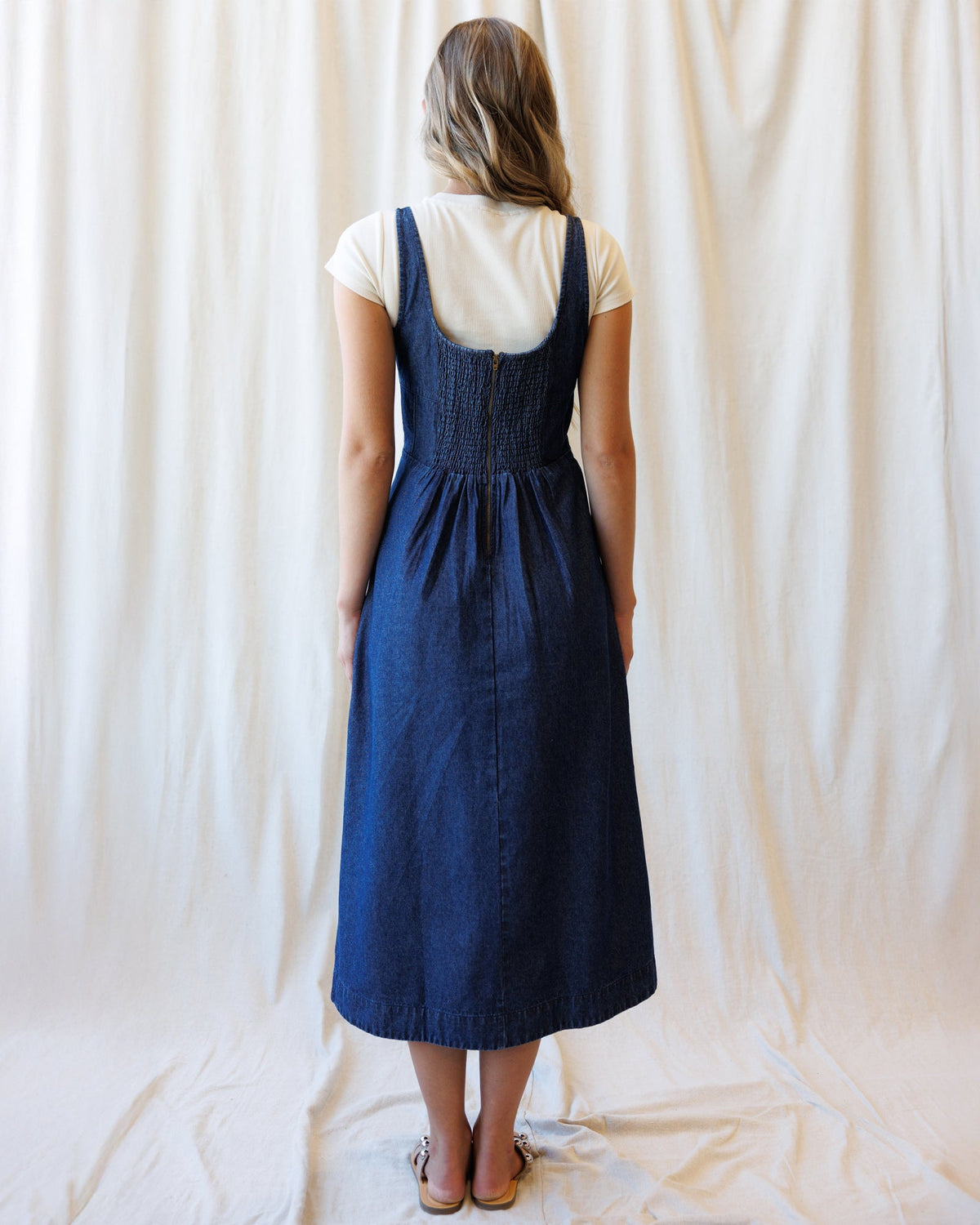 Back view of medium blue wash denim dress with smocked upper back and adjustable straps