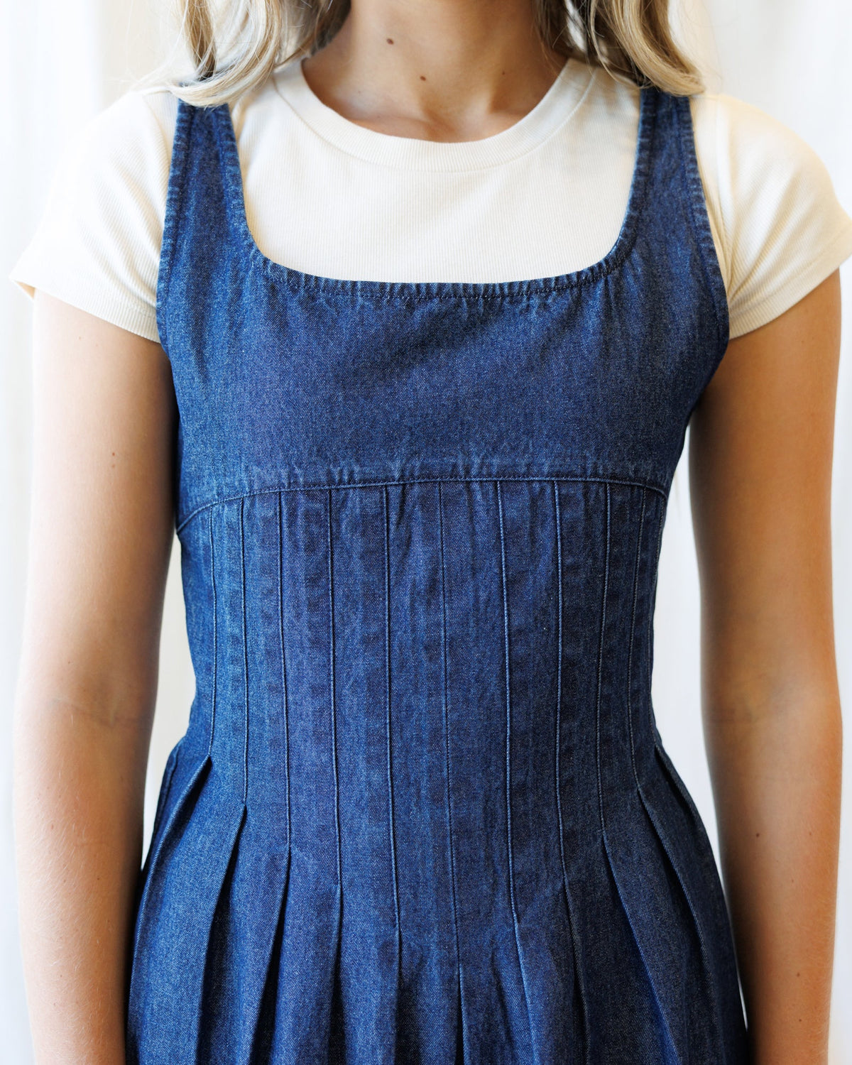 Close-up of medium blue wash denim dress bib front with gathered waist and pleated skirt