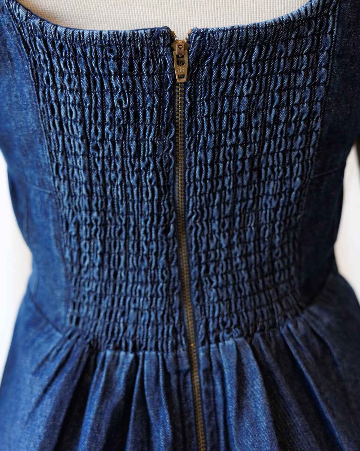 Close-up of blue denim dress smocked top with center zipper and gathered skirt hem