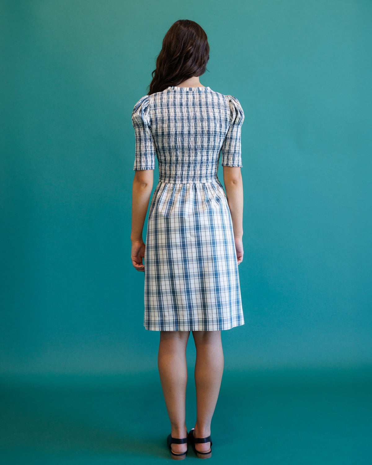 Back view of cream and blue plaid oxford dress with button closure and gathered waist.