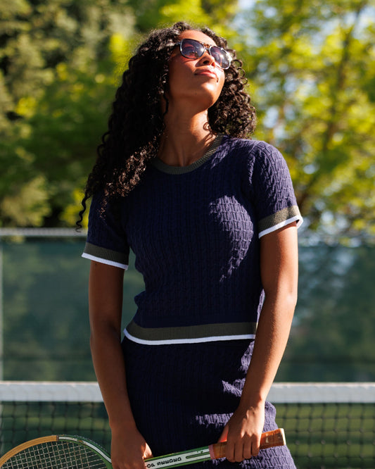 Dark blue cable-knit crew sweater with light trim at collar, cuffs, and hem