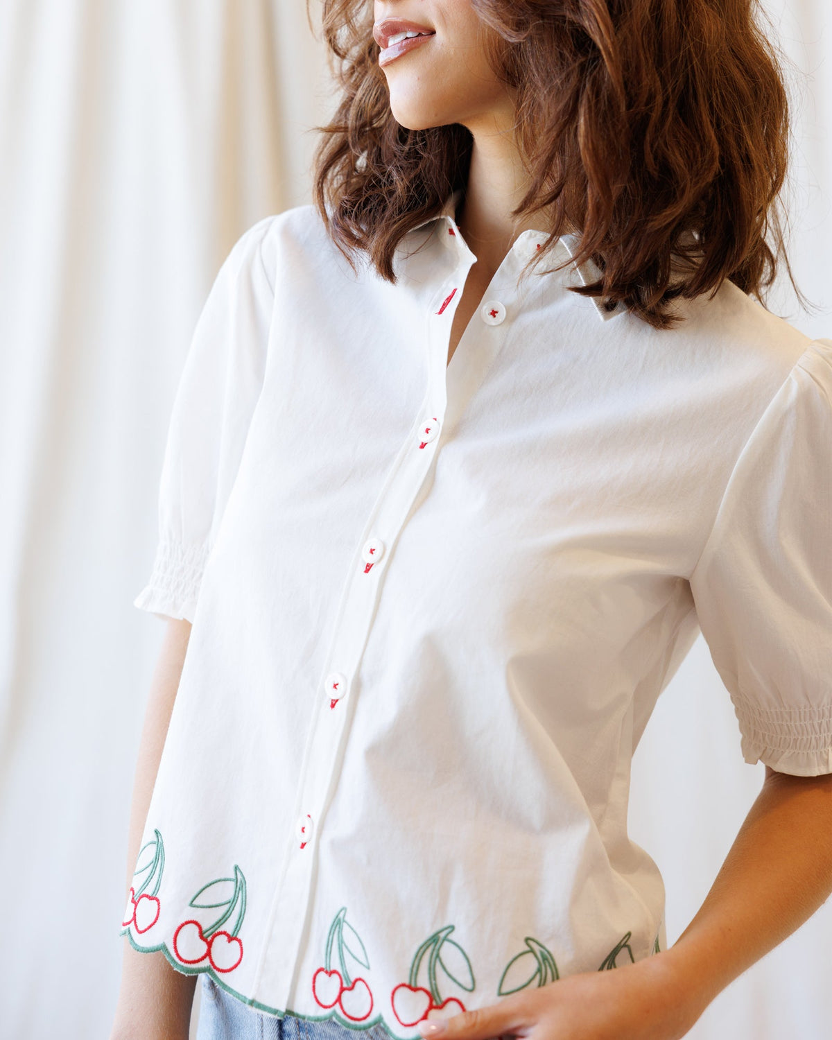 White button-down shirt close-up with red buttons and cherry-and-leaf cuff embroidery