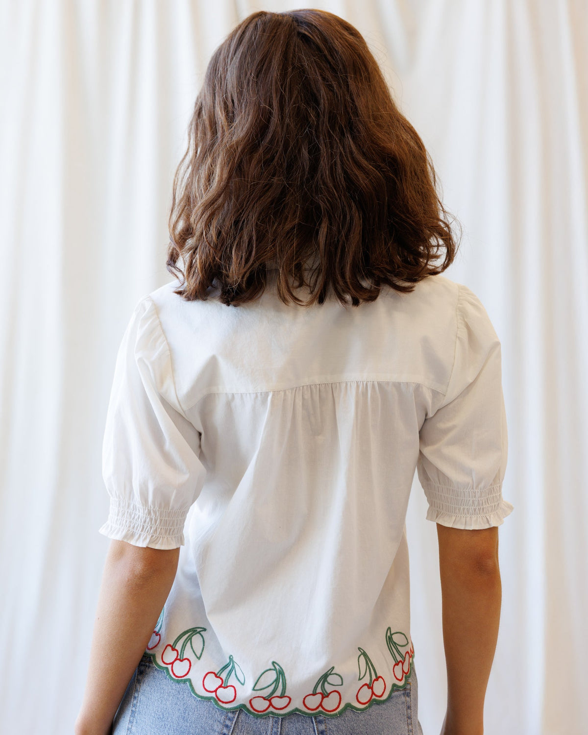 Back view of white button-down shirt with puff sleeves and cherry border embroidery