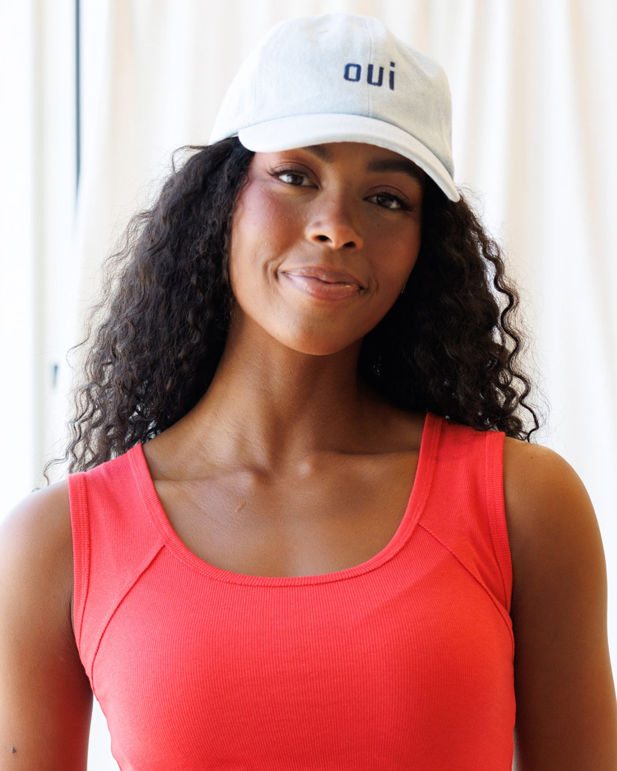 Light-blue 'oui' cap worn by woman with curly hair and sleeveless top