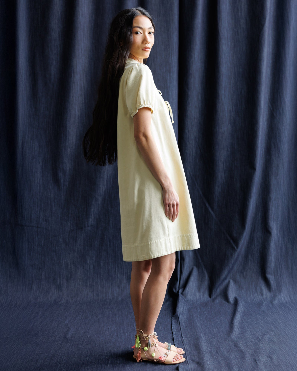 Light yellow denim dress with collared neckline ribbon bow, short puff sleeves, profile