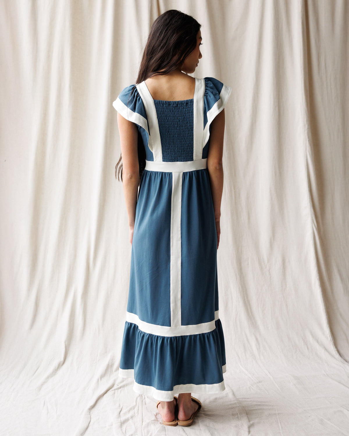 Back view of women’s Block Party dress in blue with white vertical panels and tiered hem