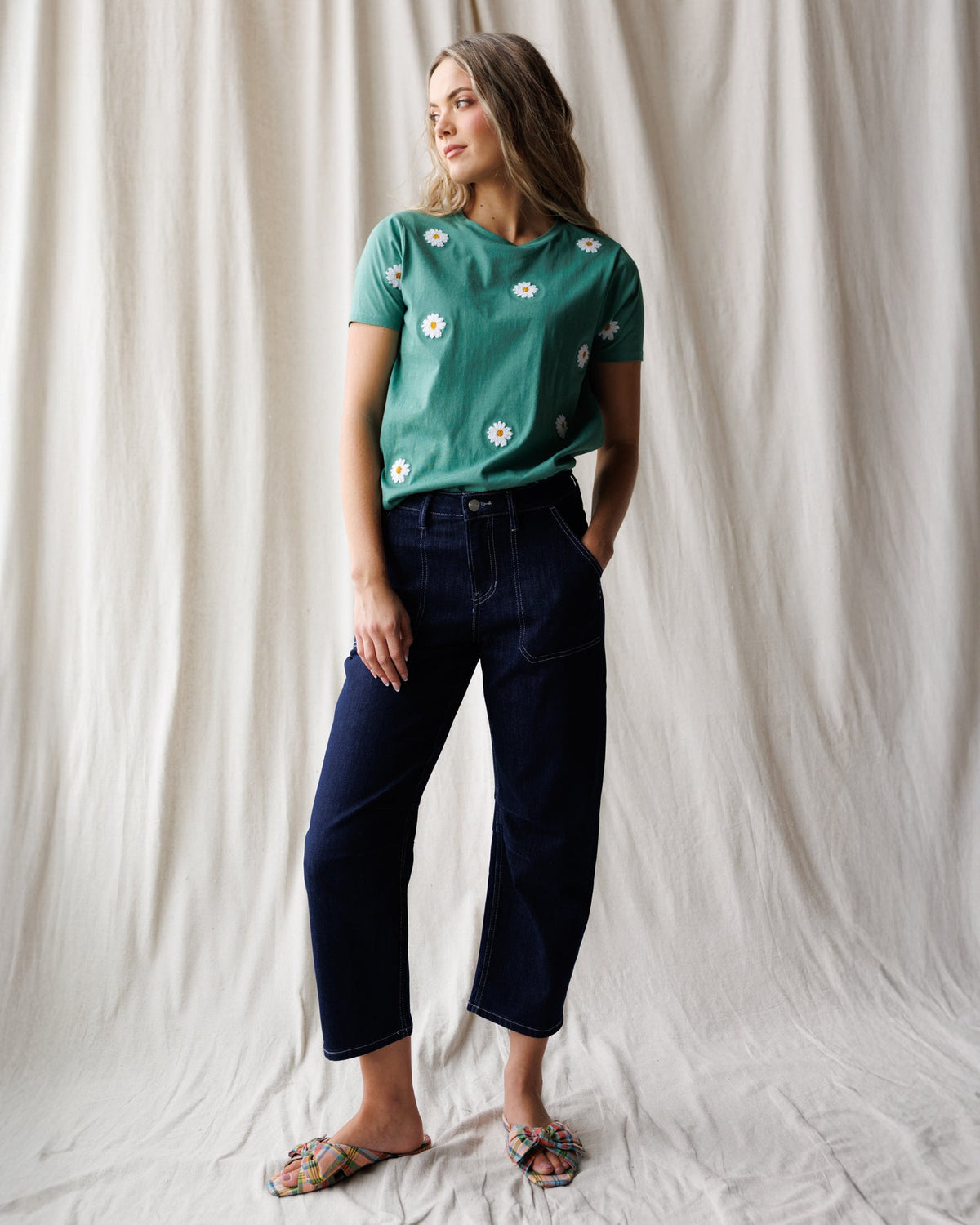 Women's teal daisy-embroidered tee with crew neck and short sleeves, styled with jeans.