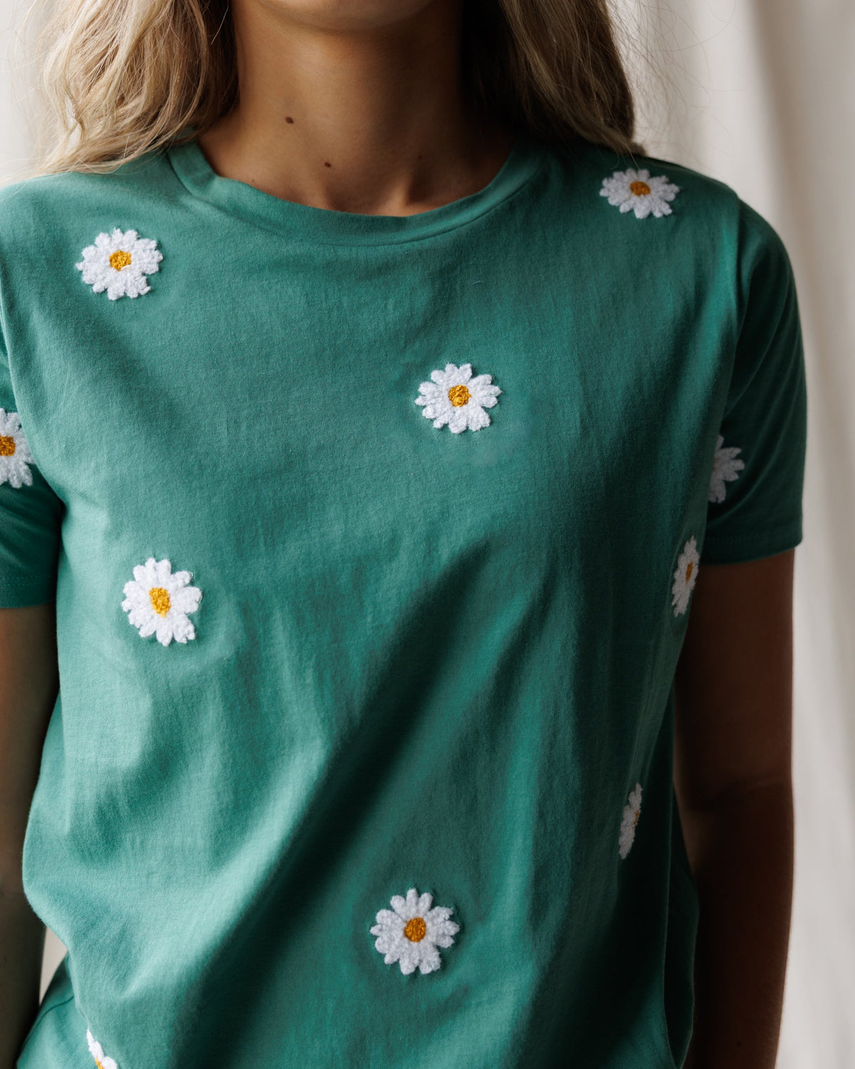 Women's teal tee with white daisy embroidery accents on the front.