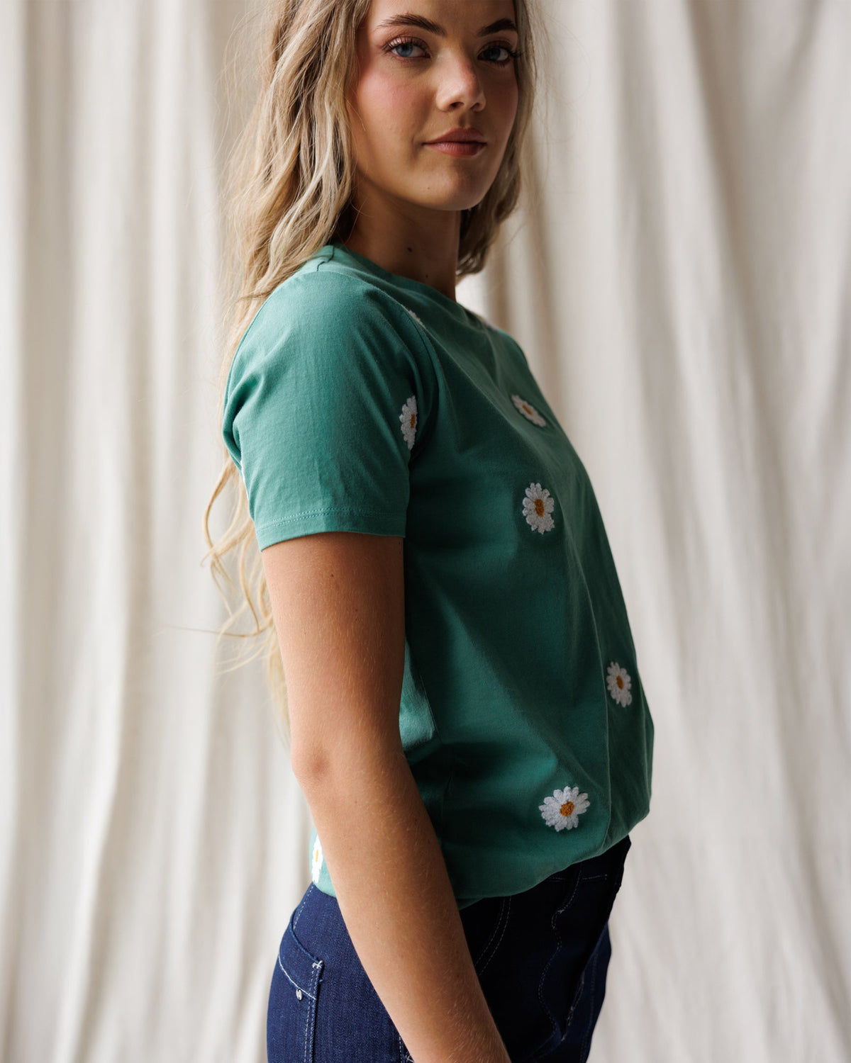 Women's teal tee with white daisy embroidery on side and sleeve.