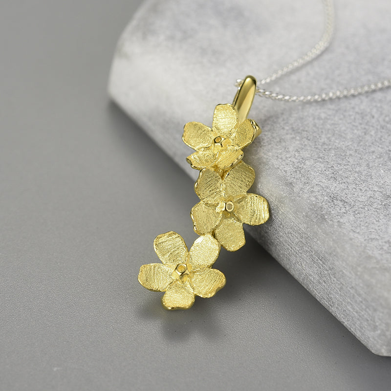Gold forget-me-not flower necklace with clustered blossoms pendant on a chain.