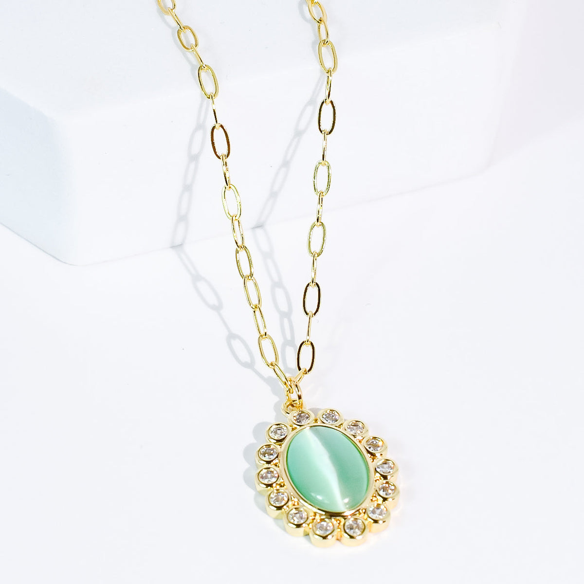 Gold-tone chain necklace with oval mint pendant, framed by rhinestone border