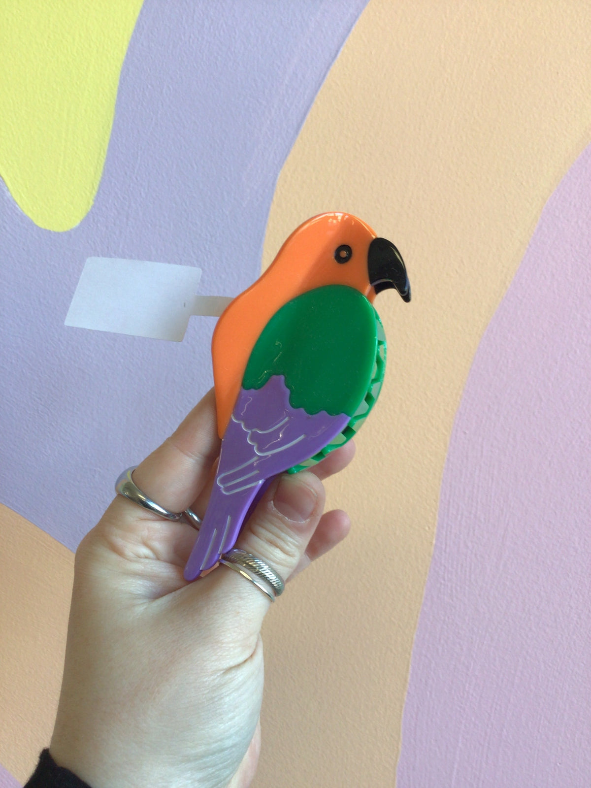 Parrot-shaped hair claw with orange head, green wing, and purple tail, glossy