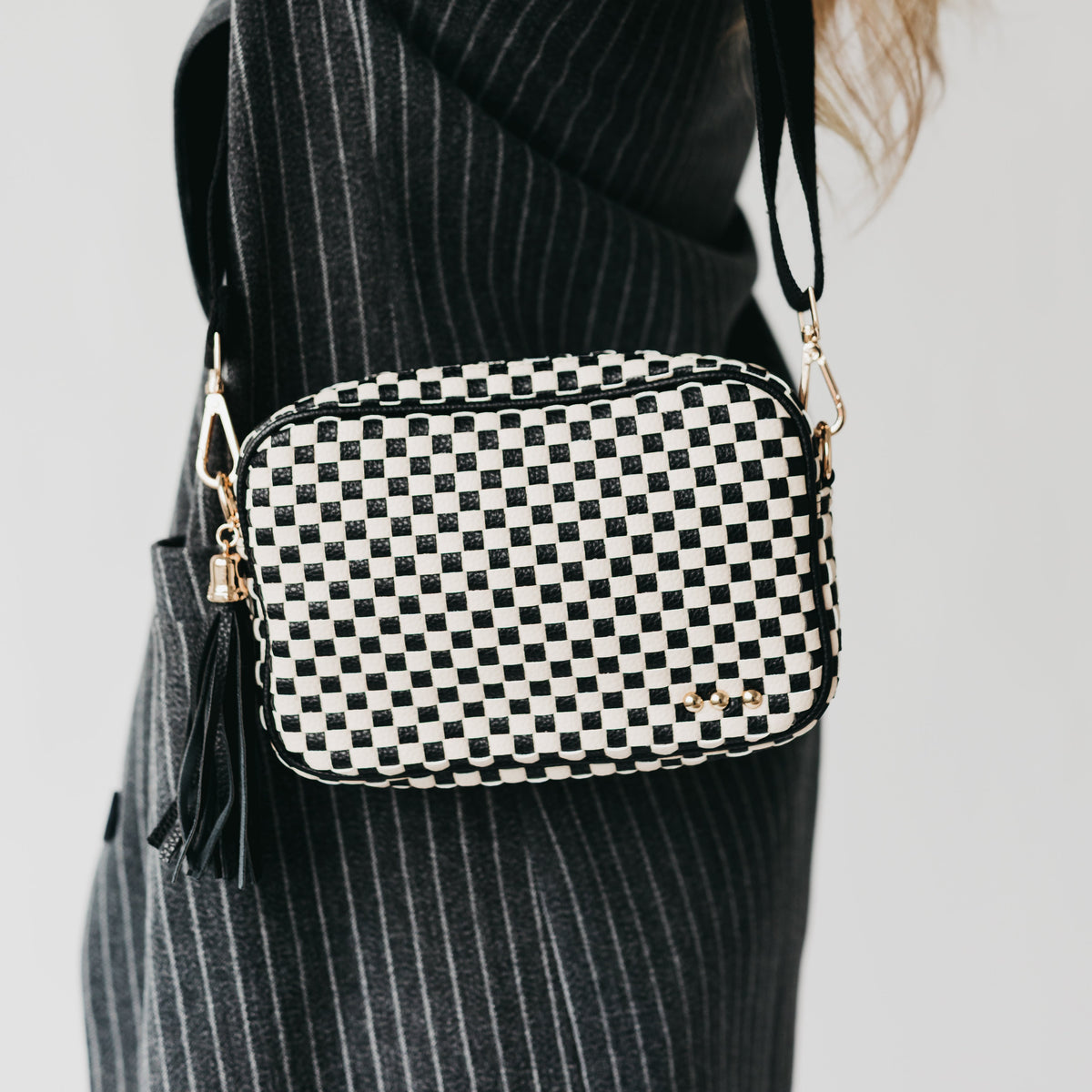 Black-and-white checkered woven crossbody bag with gold hardware and shoulder strap