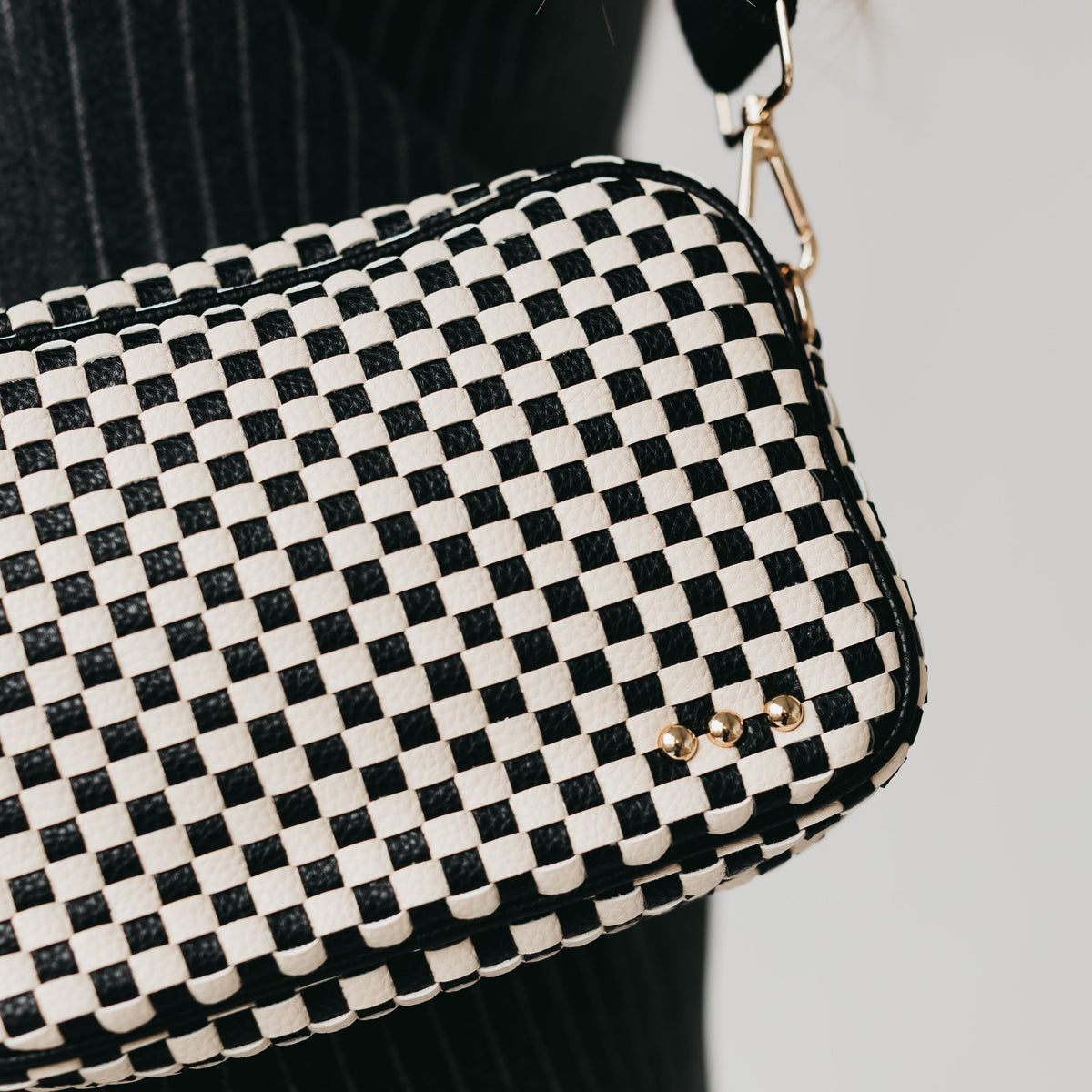 Black-and-white checkered woven crossbody bag with gold snap and decorative studs