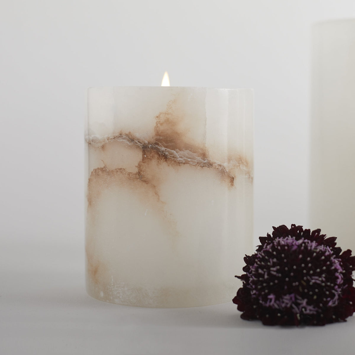 Lit short votive candle with alabaster-style marbling, white and beige veined cylinder