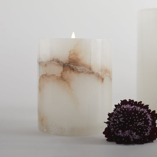 Lit short votive candle with alabaster-style marbling, white and beige veined cylinder
