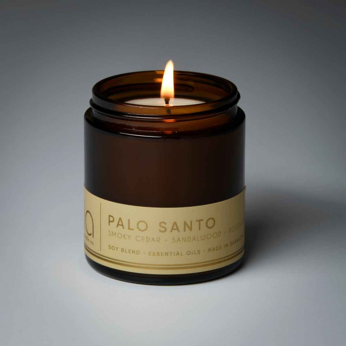 Amber glass soy candle with burning flame and “Palo Santo” label, front view