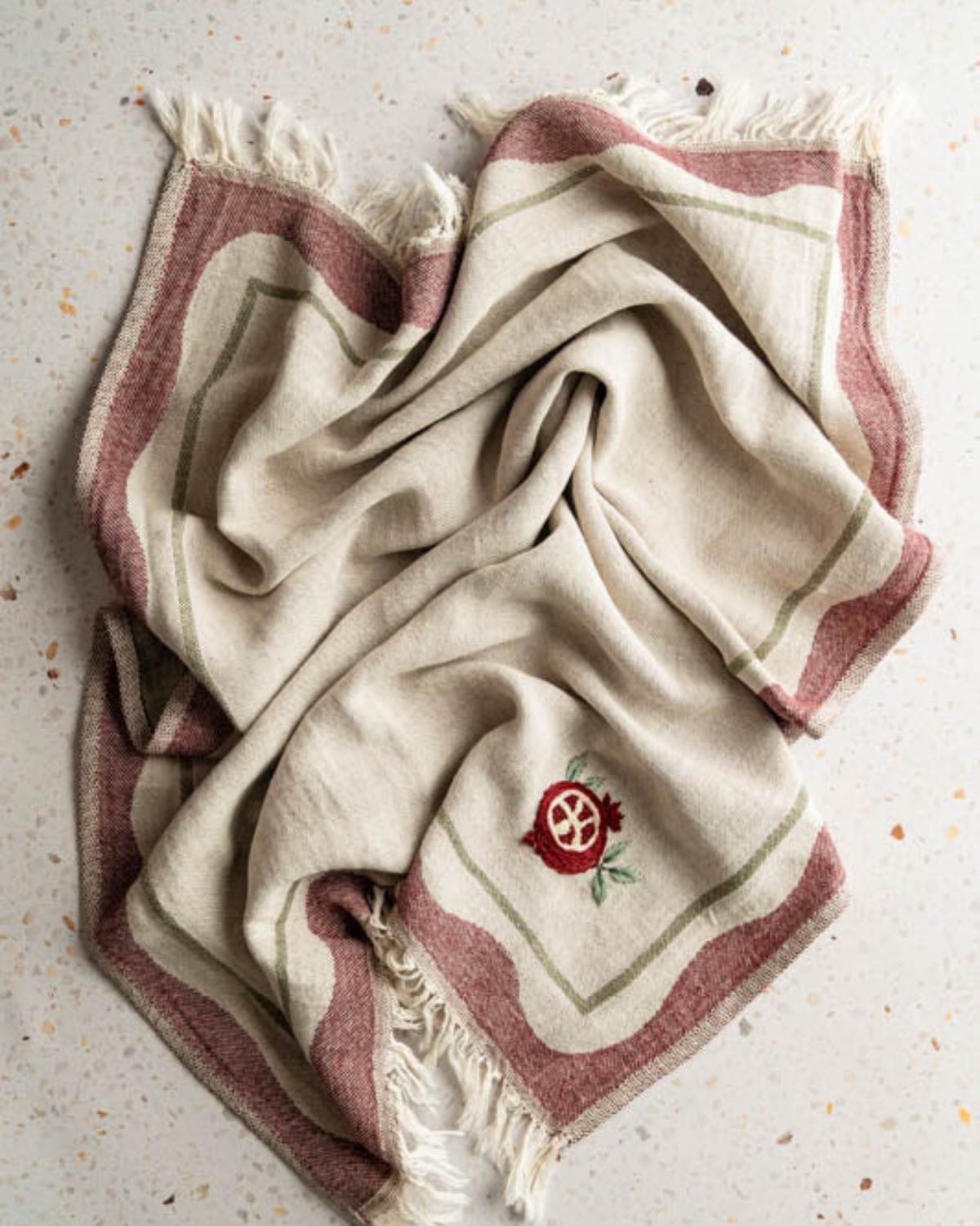 Hand-stitched towel fabric, beige folded towel with maroon stripe border and pomegranate emblem